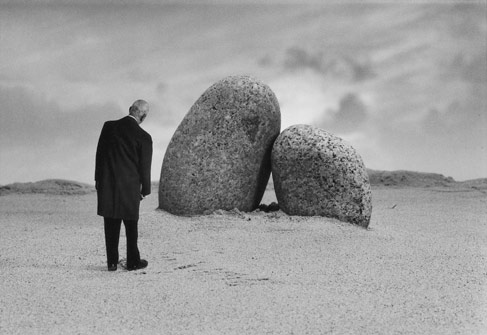 二つの岩が寄り添うように立っている前で、岩に合わせて体を傾ける男の写真